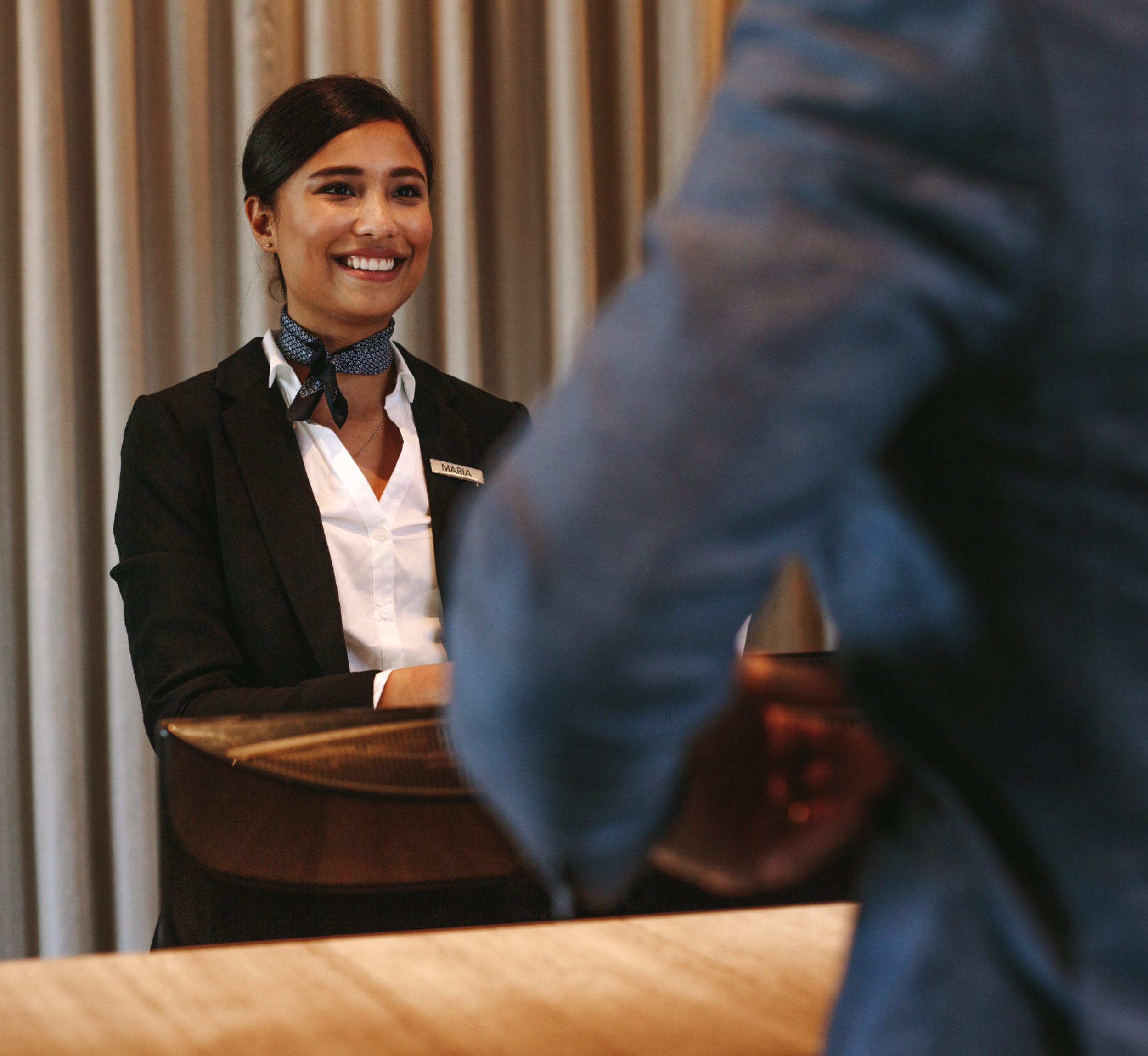 Smiling hotel receptionist talking with male guest at reception counter. Happy female receptionist worker standing at hotel counter with businessman checking in.