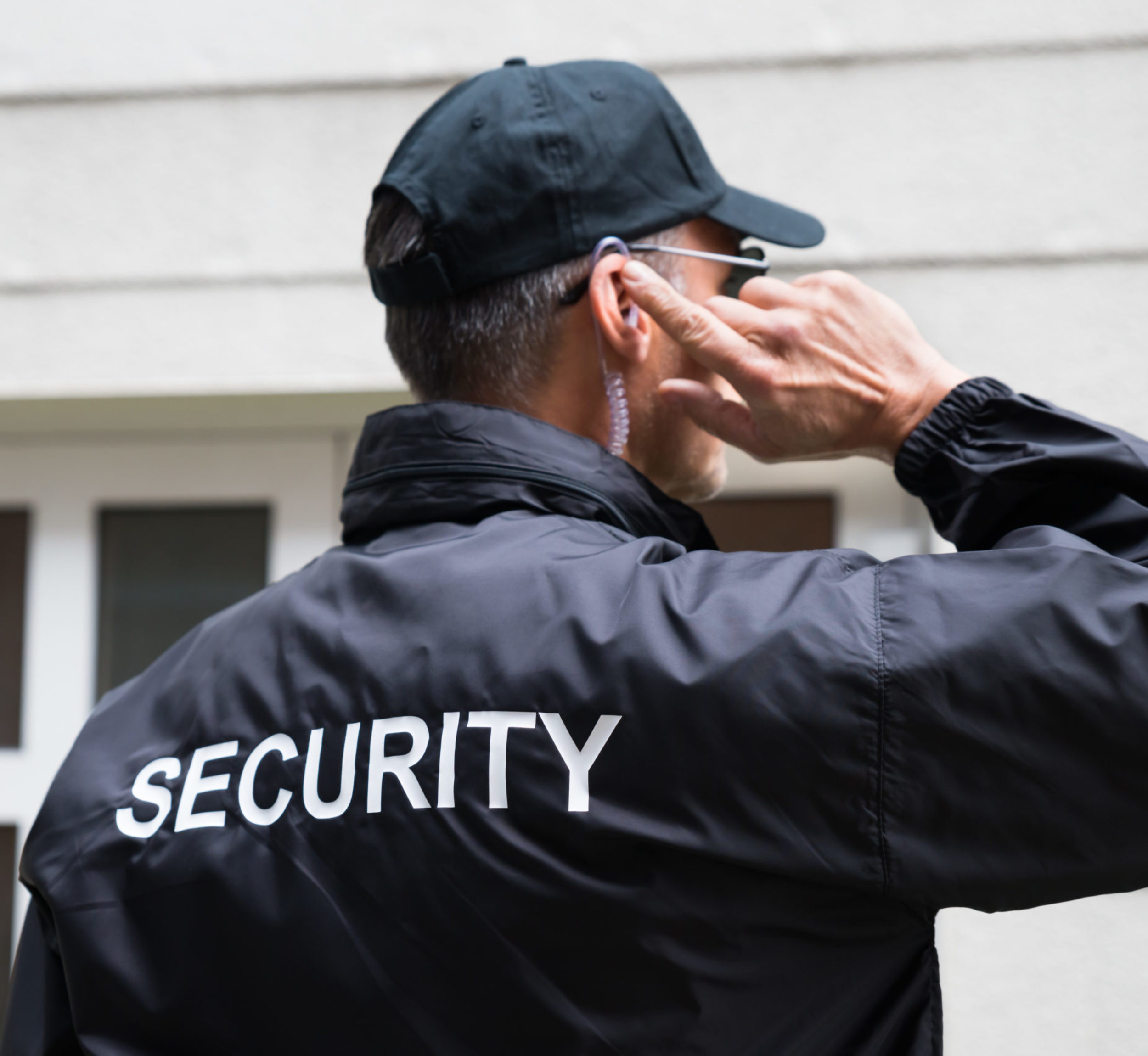 Rear view of mature security guard listening to earpiece against building