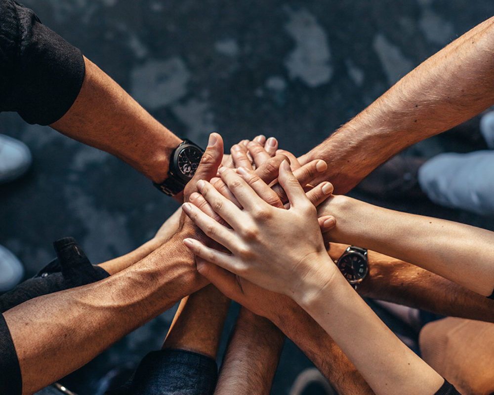 Top view of creative professionals putting their hands together as a symbol of teamwork, cooperation and unity. Stack of hands of men and woman.